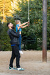 A father lifts his son up so he can hold on to the swing of a suspended rope carousel. Vertical photo