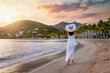A beautiful woman in a white summer dress walks down the beautiful Carlisle Bay beach, Antigua island, Caribbean Sea, during sunset time