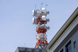 a large red and white mast on a roof with antennas and satellite dishes in front of a blue sky