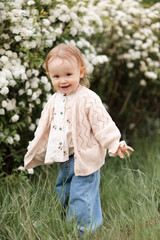 Wall Mural - Smiling cheerful baby girl 1-2 year old wearing vintage stylish clothes having fun over flowers outdoor close up. Looking at camera. Spring season.