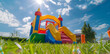 Inflatable bouncy castle on grass in a sunny day, outdoor playground with a colorful inflatable house and slide for kids