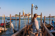 Tourist woman in dress watching gondolas moored by Saint Mark square in city Venice, Veneto, Northern Italy, Europe. Scenic view of San Giorgio di Maggiore church. Romantic vacation in Venetian Lagoon