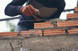 Worker hand laying bricks and using plaster trowel cement to build a house at construction site.