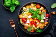 Summer vegetable salad with stale bread, tomatoes, cucumber, cheese, onion, olive oil, sea salt and green basil, black table background, top view