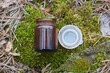one small open glass brown medical bottle with a white cap lies on green moss in nature