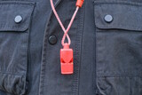 Fototapeta Desenie - one red plastic whistle on a cord hanging from black clothes on a man on the street