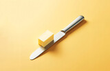 Fototapeta Londyn - A Slice of Butter on a Kitchen Knife Against a Yellow Background