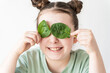Little cute funny girl using spinach instead of eyes and smiling. Concept of healthy food and vitamins.