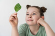 Pretty little girl holding a spinach leaf, looking at it. Concept of healthy food and natural vitamins. Selected focus.