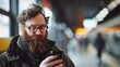 A bearded man is engrossed in his smartphone while waiting at a train station