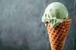 Green ice cream in a waffle cone on a gray background.