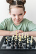 Cute little girl sitting in front of a chessboard with a cunning look. Selected focus.