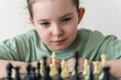 Cute little girl playing chess and looking with concentrated eyes at chessboard. Selected focus.