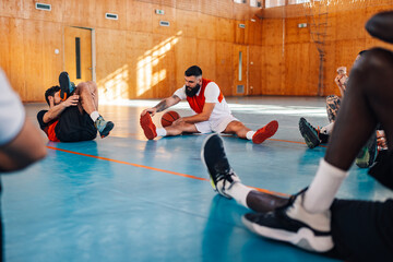 Wall Mural - Basketball player stretching his legs while sitting on a floor in a sports hall