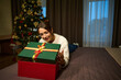Young smiling woman opening and looking inside gift box on bed during Christmas