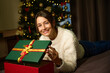 Pretty woman opening gift box and looking at camera on bed during Christmas
