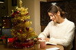 Young woman writing her wishes or notes in notebook at table during Christmas