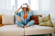 Virtual Reality Happiness: A Smiling Woman Enjoying a Futuristic VR Game at Home, Wearing VR Goggles and Sitting on a Sofa in a Modern Living Room.