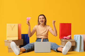 Wall Mural - Young woman with credit card and laptop shopping online on yellow background