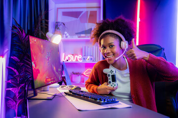 Wall Mural - African American girl gaming streamer team winner playing online fighting with Esport wearing headphones in neon lighting room. Talking other players planing strategies to win competitors. Tastemaker.