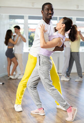 Wall Mural - Happy African american man in pair with young woman dancing and training latin dance movements in modern ballroom together