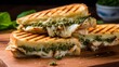 Close-up of a chicken pesto panini, with grill marks visible and basil pesto oozing out, on a cutting board. 