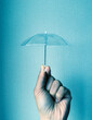 青い背景に小さなビニール傘を持っている梅雨の雨の日の湿度が高いイメージ