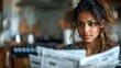 A young indian woman with an attentive gaze reading a newspaper in a warmly lit indoor setting. 