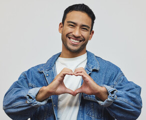 Poster - Happy, man and portrait with heart sign, fashion and love hand gesture in a studio with smile. Trendy, denim and cool outfit with confidence for valentines day with jacket and grey background