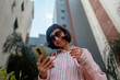 © zhukovvvlad - portrait of an elegant woman in stylish clothes with a smartphone on a city street. Happy business woman using phone and headphones outdoors.