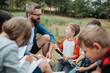 © Halfpoint - Young students learning about nature, forest ecosystem during biology field teaching class, writing notes. Teachers talking with children during outdoor active education.