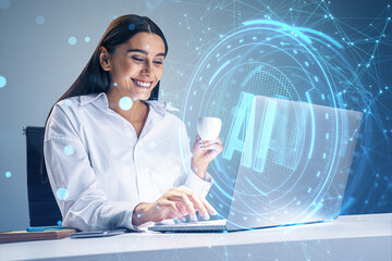 Poster - Happy young businesswoman with coffee cup using laptop at desk with glowing blue AI hologram on blurry background. Artificial intelligence, technology and innovation concept.