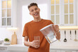 Happy man pouring water from filter jug into glass in kitchen