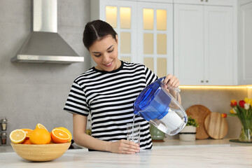 Canvas Print - Woman pouring water from filter jug into glass in kitchen