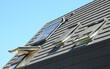 Asphalt shingles house roof top with attic skylights, open windows, dormer, solar water heater and solar panels.
