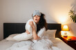 © _KUBE_ - Tired Caucasian woman wearing sleep mask sitting in bed with pillow and can't sleep. Concept of insomnia and sleepless