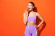 Young happy fitness trainer instructor sporty woman sportsman wear purple top clothes in home gym hold measure tape eat bite apple isolated on plain orange background. Workout sport fit abs concept.