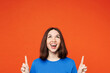 Young smiling happy cheerful woman wear blue t-shirt casual clothes point index finger overhead on area copy space mock up isolated on plain red orange background studio portrait. Lifestyle concept.
