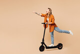 Fototapeta  - Full body side view young woman wear orange shirt casual clothes ride electric scooter do super hero power gesture isolated on plain pastel light beige background studio portrait. Lifestyle concept.