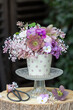 Blumenarrangement mit Lenzrosen, Fliederblüten, Hornveilchen und Maßliebchen im Porzellanbecher