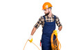 © deagreez - Half face portrait of busy stylish electrician with stubble in overall, shirt, hardhat installing, laying a cable, having rolled wire in hand, standing over grey background