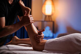 Fototapeta Łazienka - Masseuse makes an anticellulite relaxing foot massage in a spa for a young girl in a comfortable atmosphere with evening light. Therapeutic foot massage, recovery after injuries, health maintenance.
