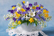 Bouquet of wild spring flowers in a cup, blue muscari, hepatica, pansies, yellow anemones, white bird cherry. Beautiful card