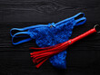 Red whip and blue panty for adult role play games over black wooden background