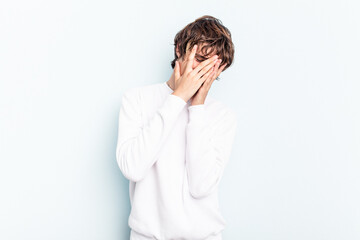 Wall Mural - Young caucasian man isolated on blue background blink at the camera through fingers, embarrassed covering face.