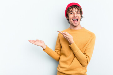 Poster - Young caucasian man isolated on blue background excited holding a copy space on palm.