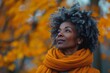 An elegant older woman with stylish curly gray hair poses against a backdrop of beautiful autumn leaves