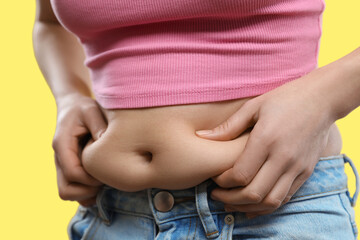 Poster - Woman touching belly fat on yellow background, closeup. Overweight problem