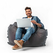 © KimlyPNG - Full length happy young man sit in bag chair unboxing new laptop on transparency background PSD