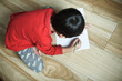 Little asian boy sitting on ground and drawing on paper